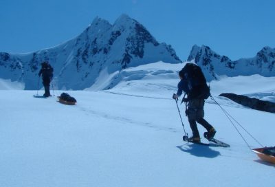 Backcountry skiers pulling sleds across a snowy alpine landscape