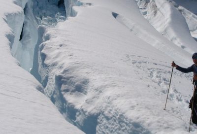 Two mountaineers crossing a steep snow slope near a large crevasse, practicing glacier travel, hazard recognition, and safe route selection.