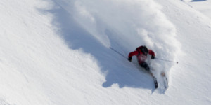 Backcountry skier navigating a steep powder face during advanced heli-ski guide training in Alaska’s high-alpine terrain.