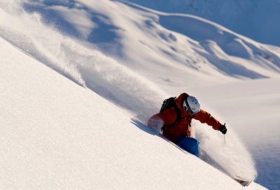 A heli-skier descends a steep powder slope in the mountains of Southeast Alaska, showcasing advanced backcountry terrain.