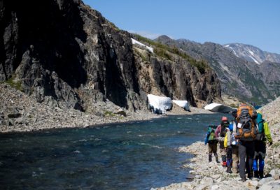 A group of hikers follows a narrow trail along the edge of a river on the Chilkoot Trail in Southeast Alaska.