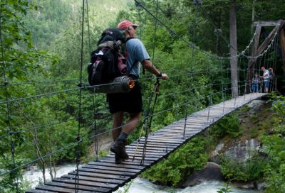 A hiker walks across a wooden bridge spanning a fast-flowing river in Southeast Alaska.