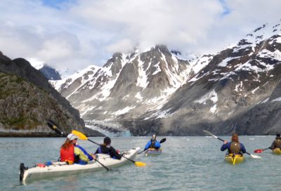 Kayakers on Alaska waters toward snow-covered mountains in Glacier Bay
