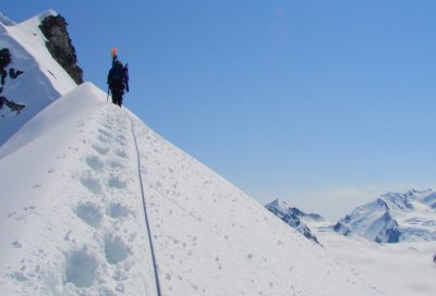 Roped climber walking along a snowy mountain ridge.