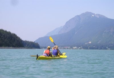 Couple kayaking in Lynn Canal overlooking the town of Haines and rugged coastal peaks.