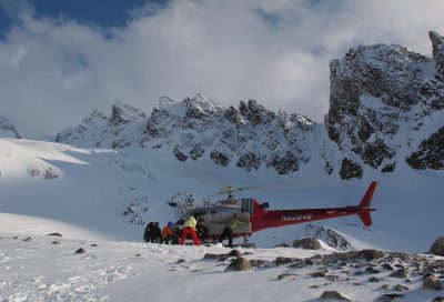 Skiers unloading gear from a helicopter on a backcountry heli-ski drop-off in Alaska.