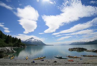 Kayaking launch site near Glacier Bay with calm waters, mountains, and expedition gear.