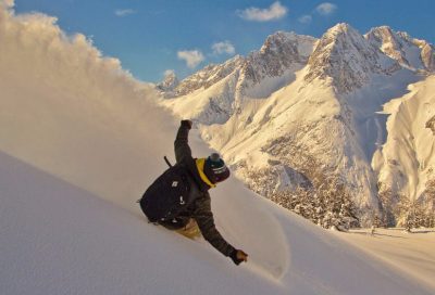 Snowboarder carving deep powder during a heli-snowboard expedition in the Alaska backcountry.