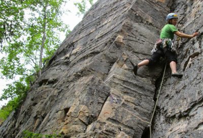 Climber placing gear and navigating a crack system on a granite cliff in Alaska.
