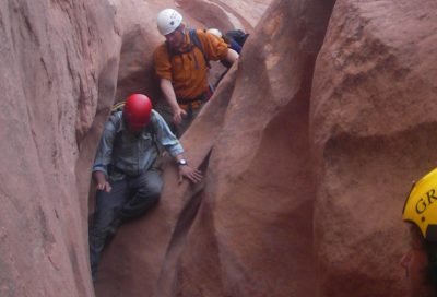 Canyoneering students navigating a narrow sandstone slot canyon in Utah.