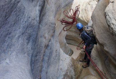 Canyoneer preparing to rappel through a narrow sandstone slot canyon in Utah.