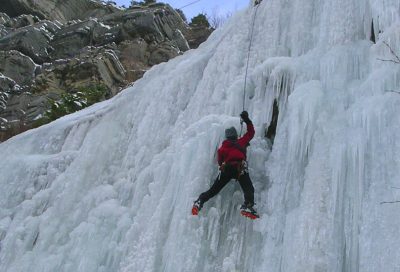 Ice climber ascending a vertical frozen waterfall in Utah using crampons and ice tools.