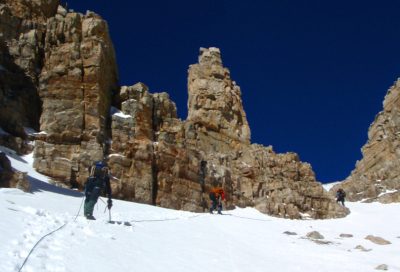 Mountaineers climbing a steep snow slope surrounded by rugged Utah rock formations.