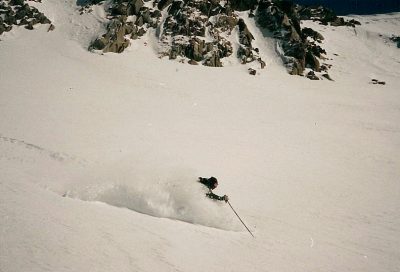Backcountry skier dropping into fresh snow below rocky ridges in Utah.