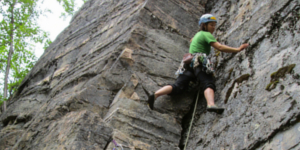 Climber placing protection while scaling a natural rock wall in Alaska.