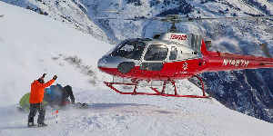 Skiers and helicopter on a snowy ridge during Alaska heli-skiing.
