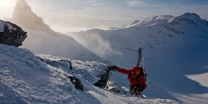 Mountaineer ascending a steep snowy ridge at sunrise.