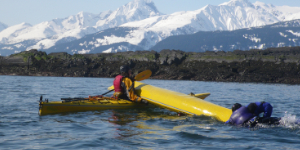 Kayakers performing a rescue drill with a capsized kayak in Alaska waters.